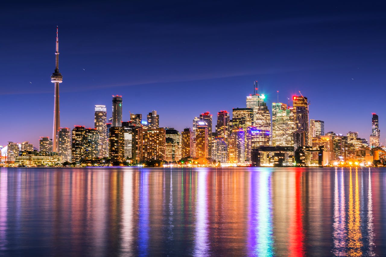 services-04 Illuminated Toronto skyline with CN Tower reflecting on calm water under a clear night sky.